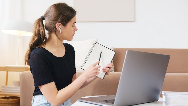 Female student engaging in online learning with laptop and notebook at home.